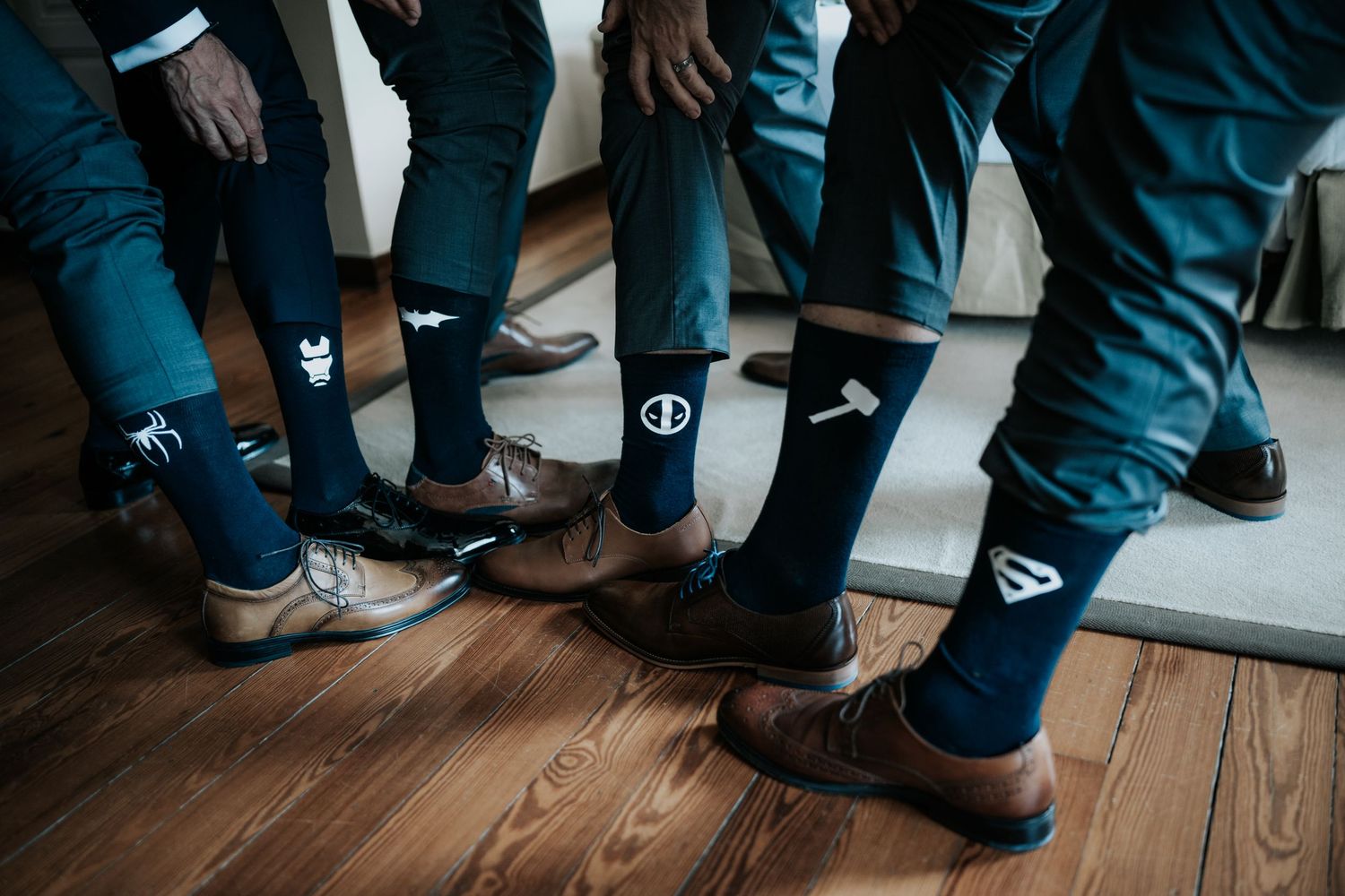 Groomsmen wearing matching navy socks and dress shoes stand together on hardwood floor.