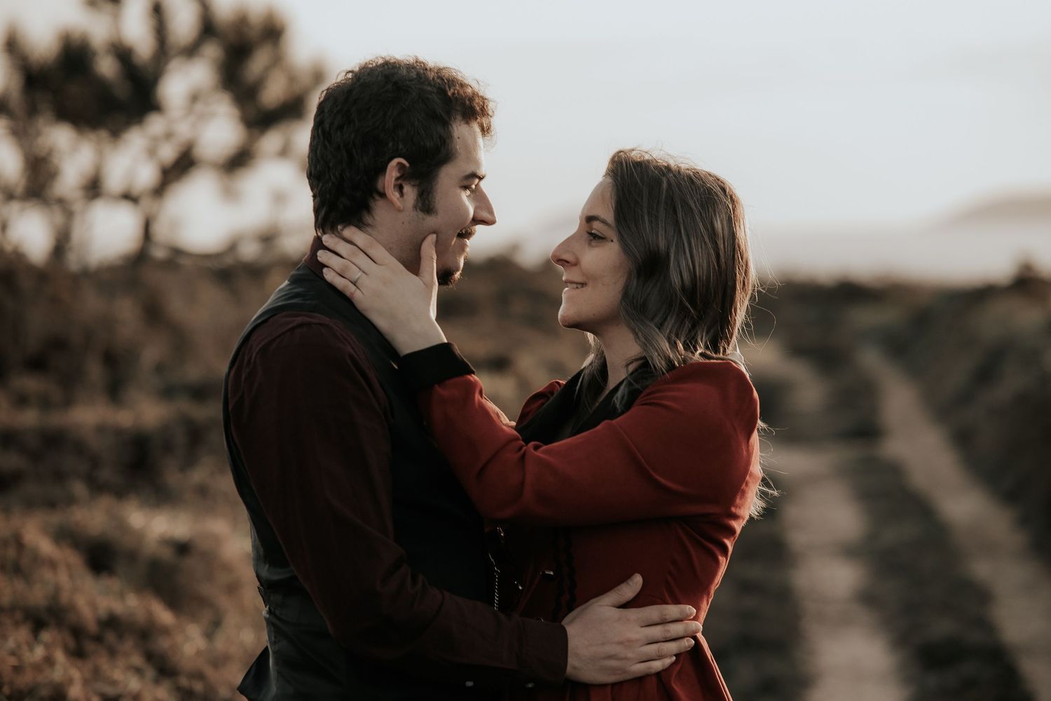 A romantic couple embraces in a sepia-toned outdoor setting with mountains in the background.