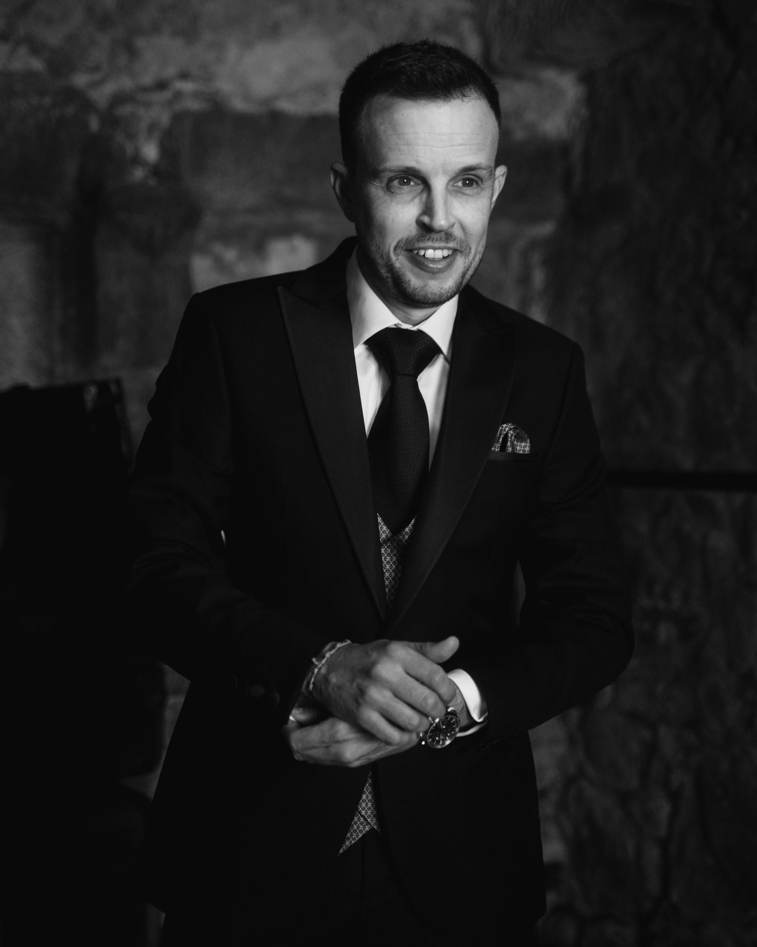 Black and white portrait of a person in a formal suit and tie against a textured backdrop.