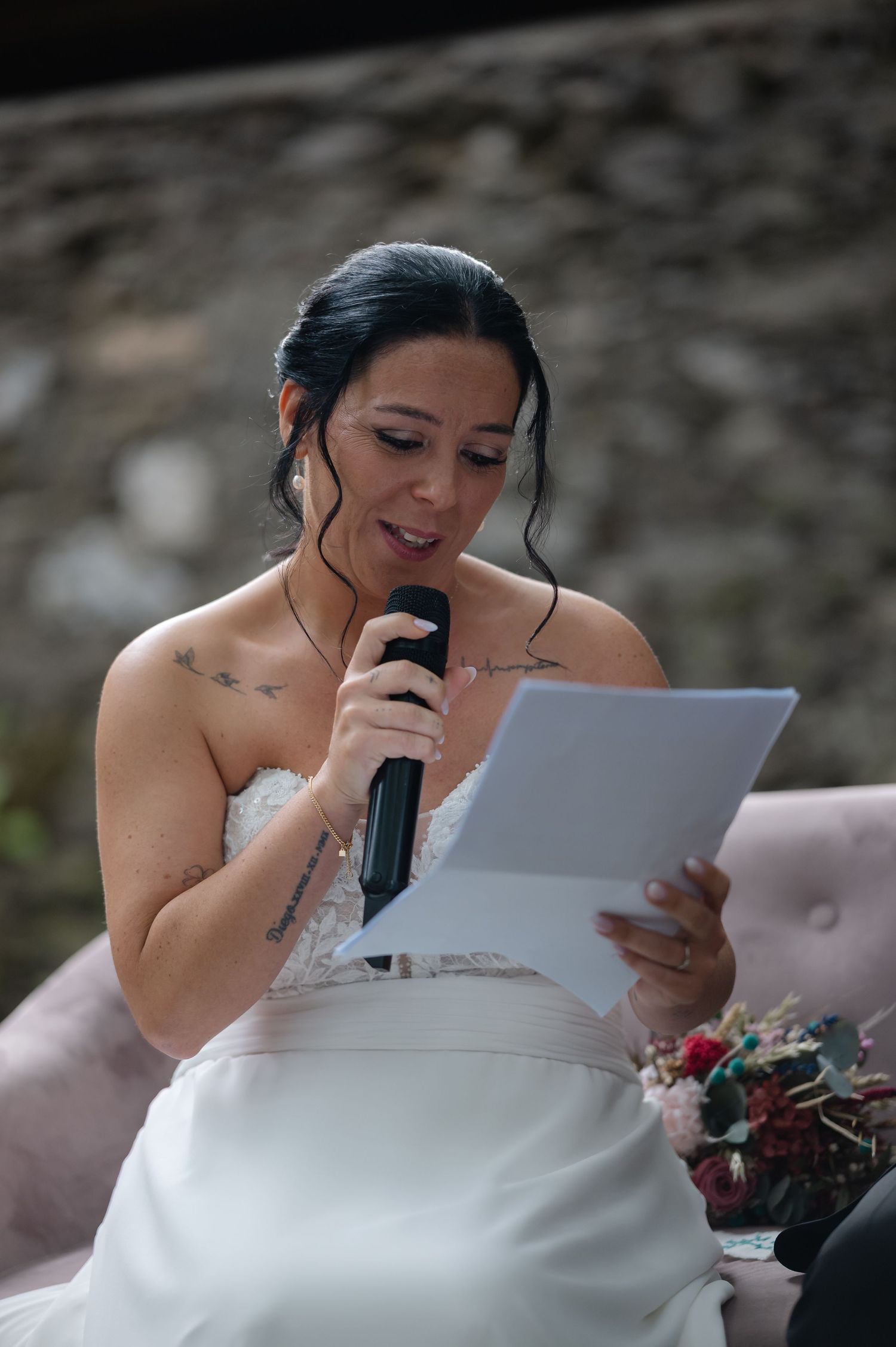 A bride in a white strapless dress reads from papers during an emotional wedding ceremony speech.