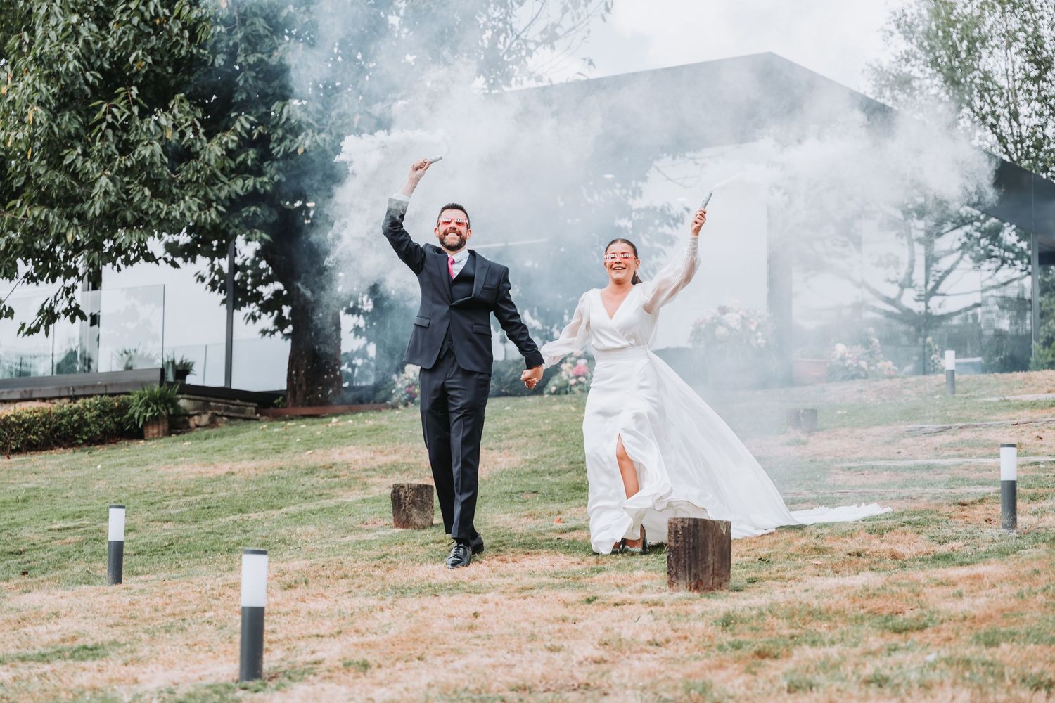 A couple joyfully runs through a misty outdoor setting on their wedding day with the bride's veil flowing in the breeze.
