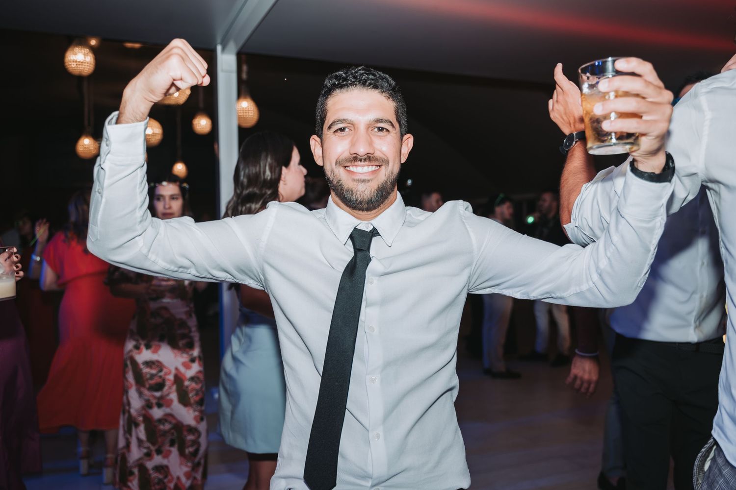 Wedding guests dancing and celebrating with raised arms on a lively dance floor at a reception party.