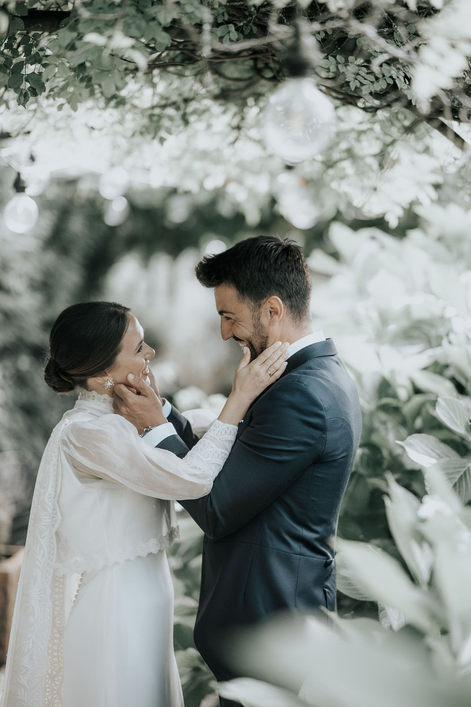 A romantic wedding moment captured through blossoming tree branches in a dreamy outdoor setting.