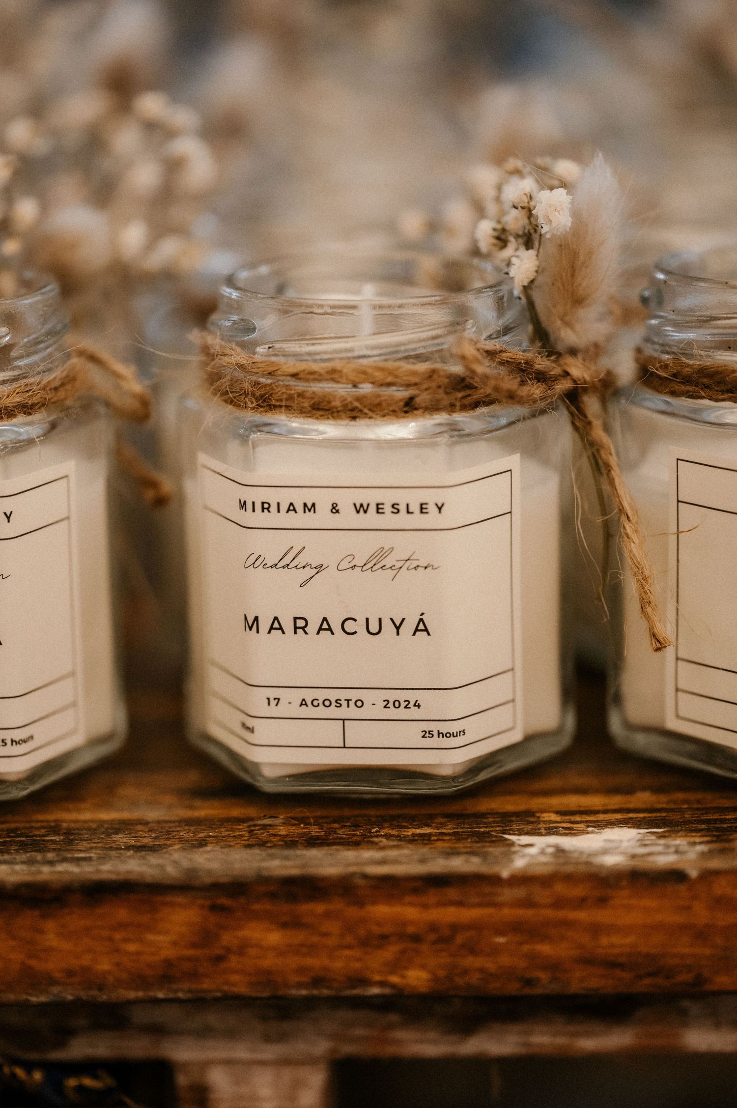 Rustic wooden shelf displays elegant glass candle jars with minimalist white labels showing names and dates.
