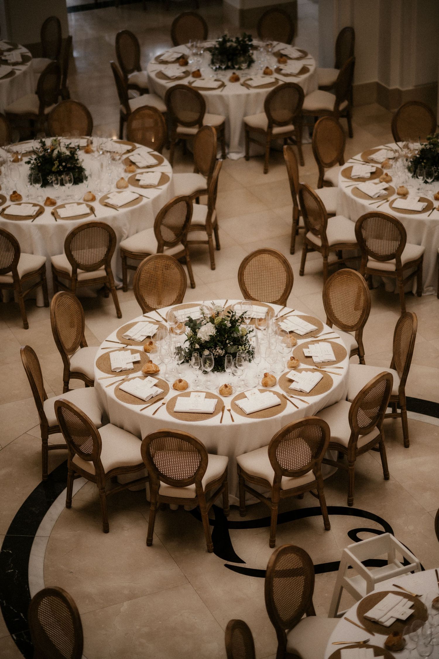 Elegant banquet hall setup with round tables, white tablecloths, and classic wooden chairs in a warm sepia tone.