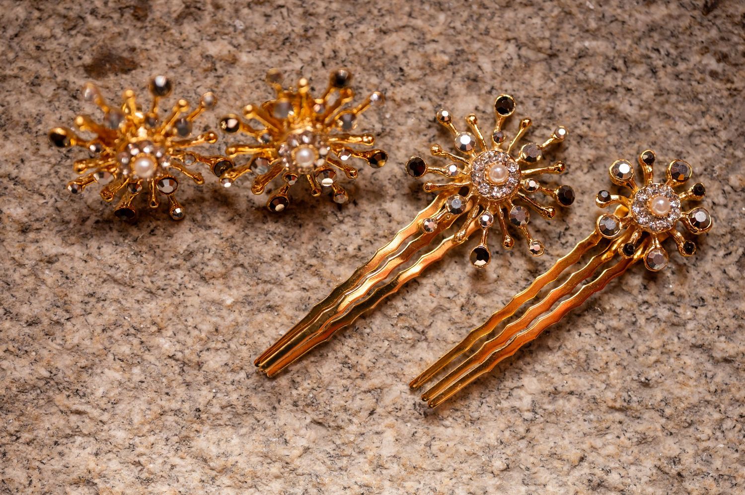 Ornate gold hair accessories and clips with pearl and crystal embellishments arranged on textured surface.