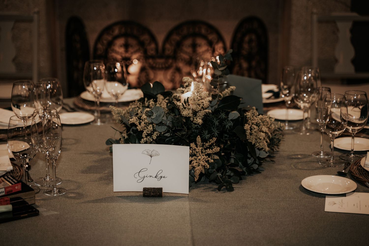Elegant wedding reception table settings with white plates, wine glasses, and moody ambient lighting.