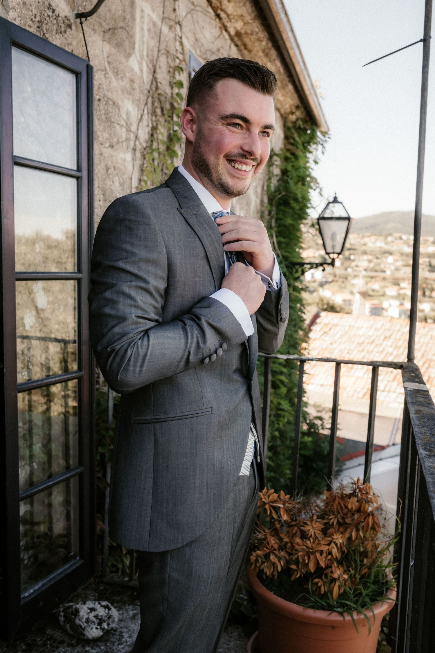 Four sequential shots of someone in a gray suit standing on a balcony with stone walls and mountain views.