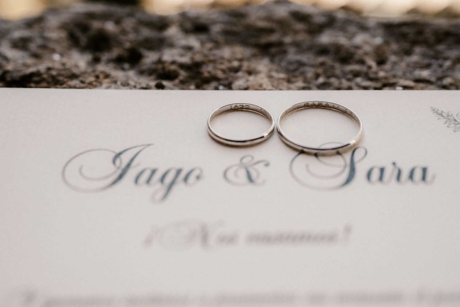 Two silver wedding rings displayed on an elegant invitation card with calligraphy text.