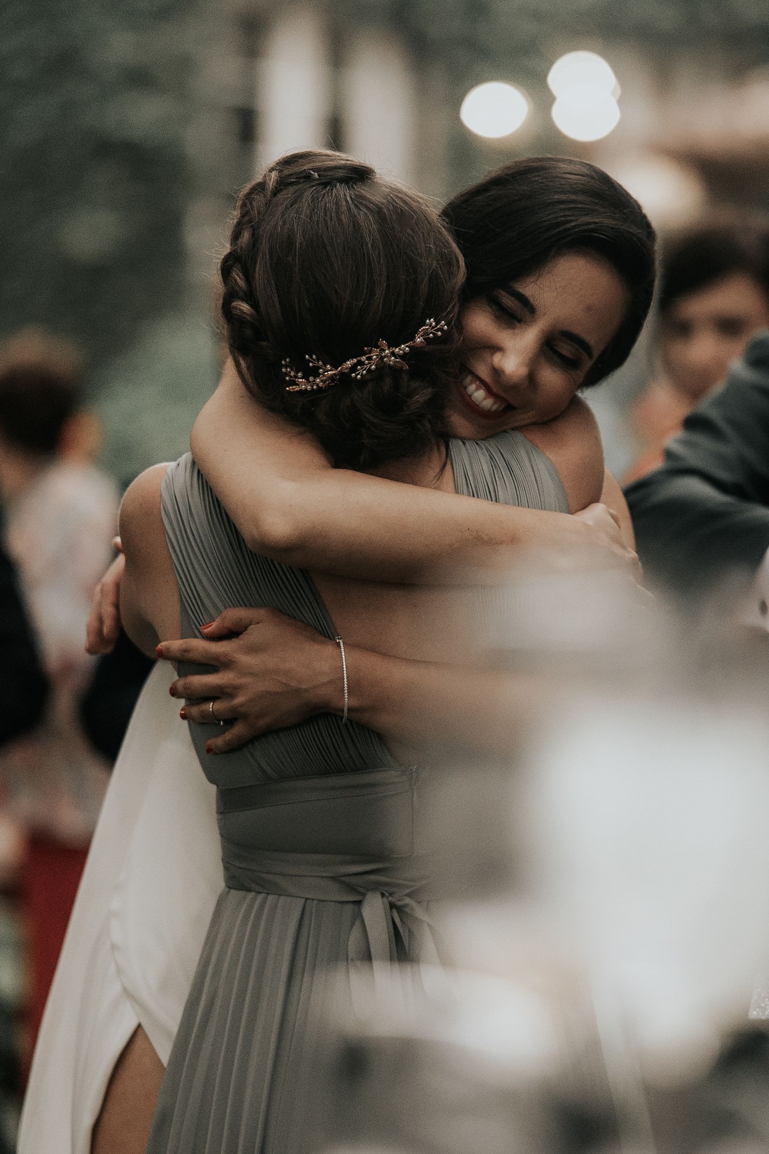 Wedding party members share emotional embraces during an outdoor celebration in muted earth tones.
