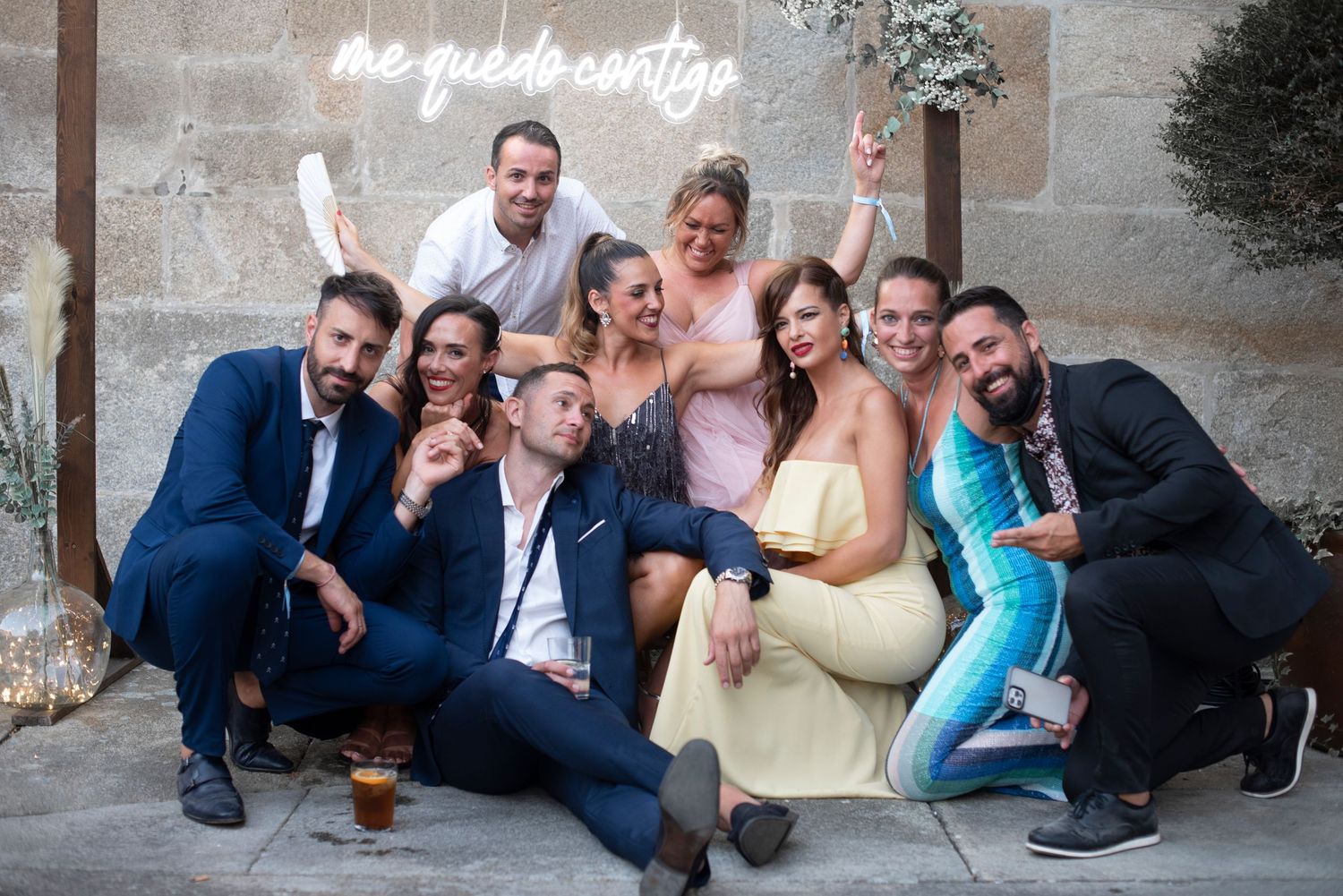 Wedding guests pose playfully in a series of candid photo booth style shots against a stone wall.