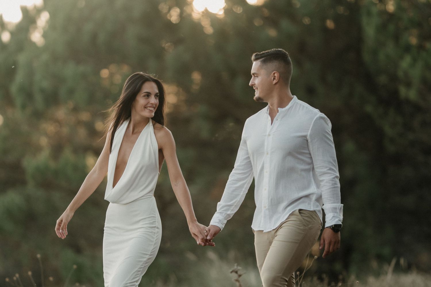 Romantic couple holding hands while walking together in a dreamy outdoor setting at sunset.