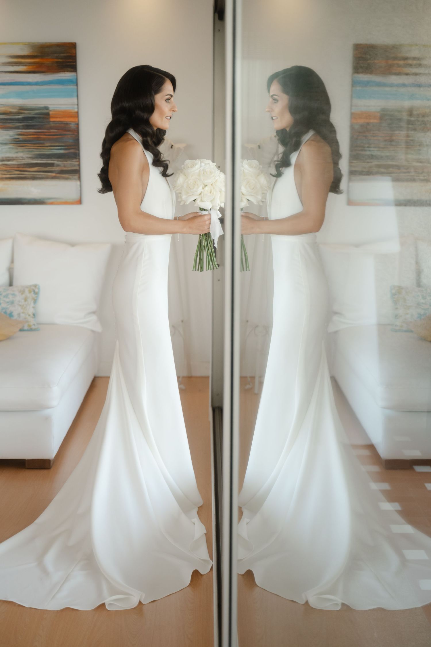 Elegant white wedding dress shown in multiple reflection angles against a mirrored wall with abstract art.