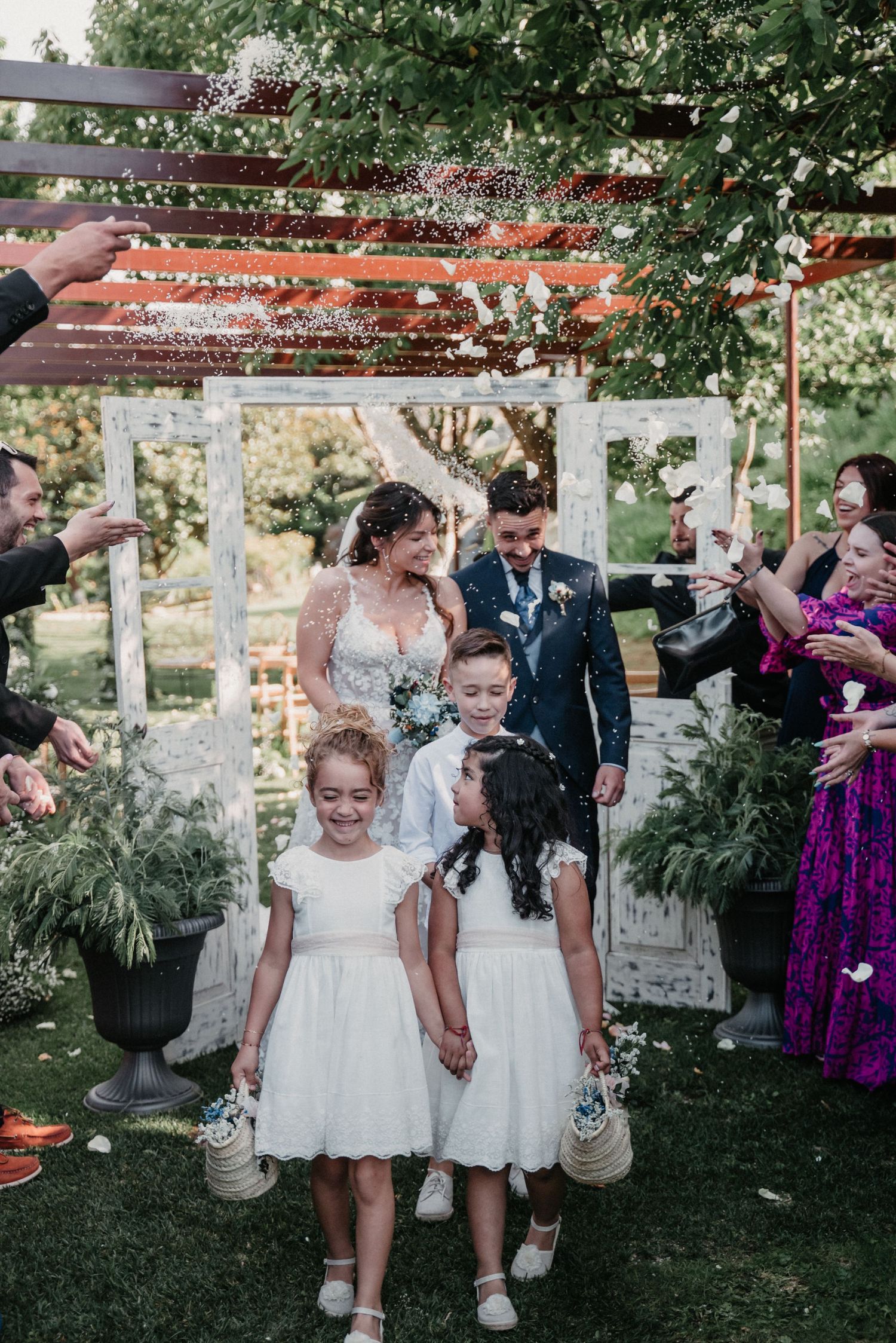 Wedding celebration with flower girls in white dresses walking under decorative streamers.