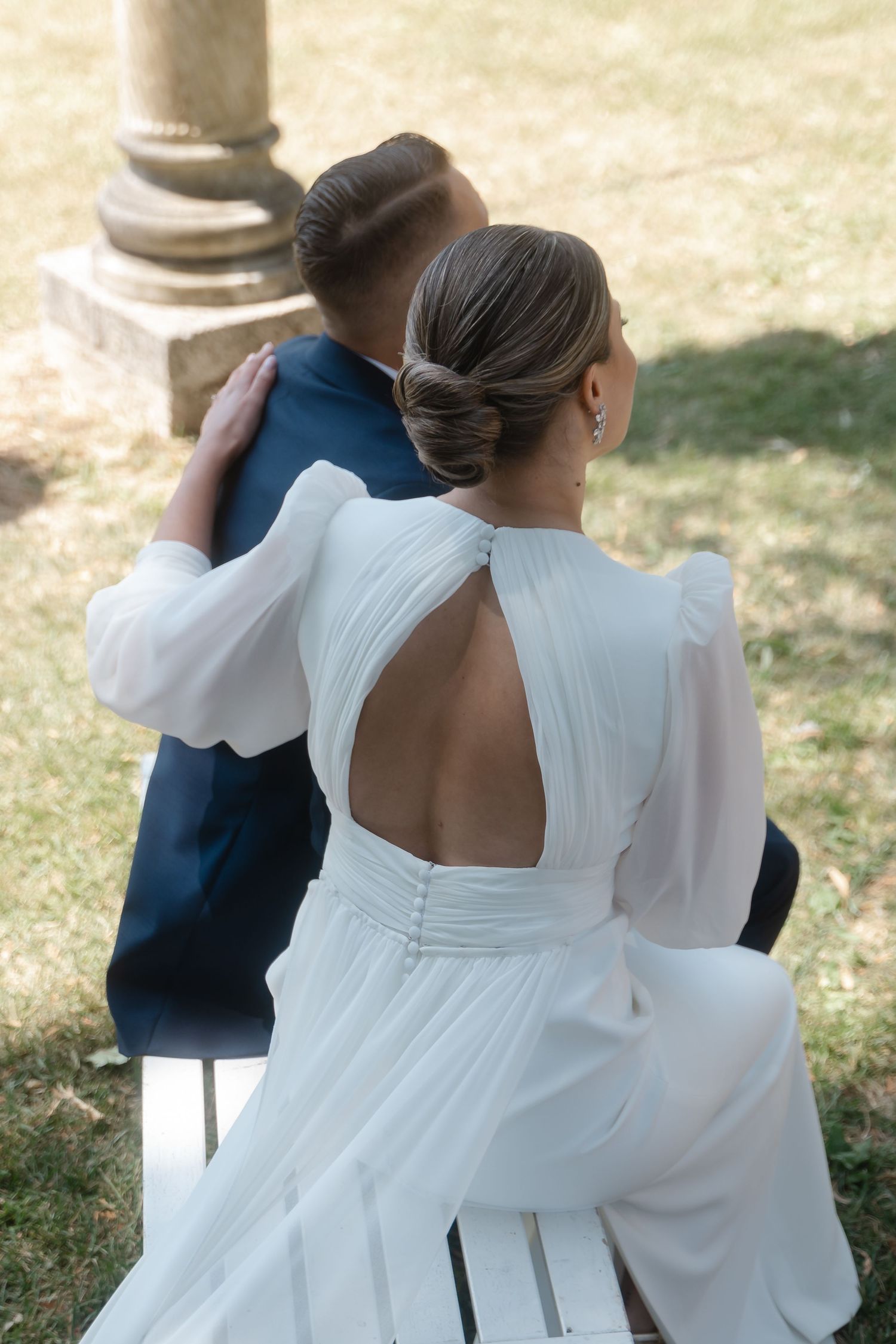 Back view of bride in white dress standing outdoors during daytime ceremony.