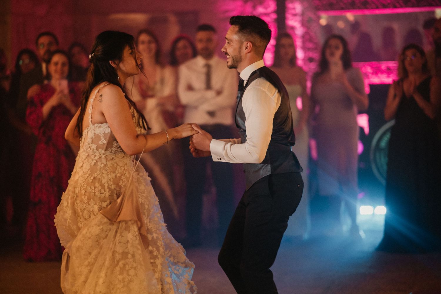 A couple dances together at a wedding reception with pink and blue lighting creating a romantic atmosphere.