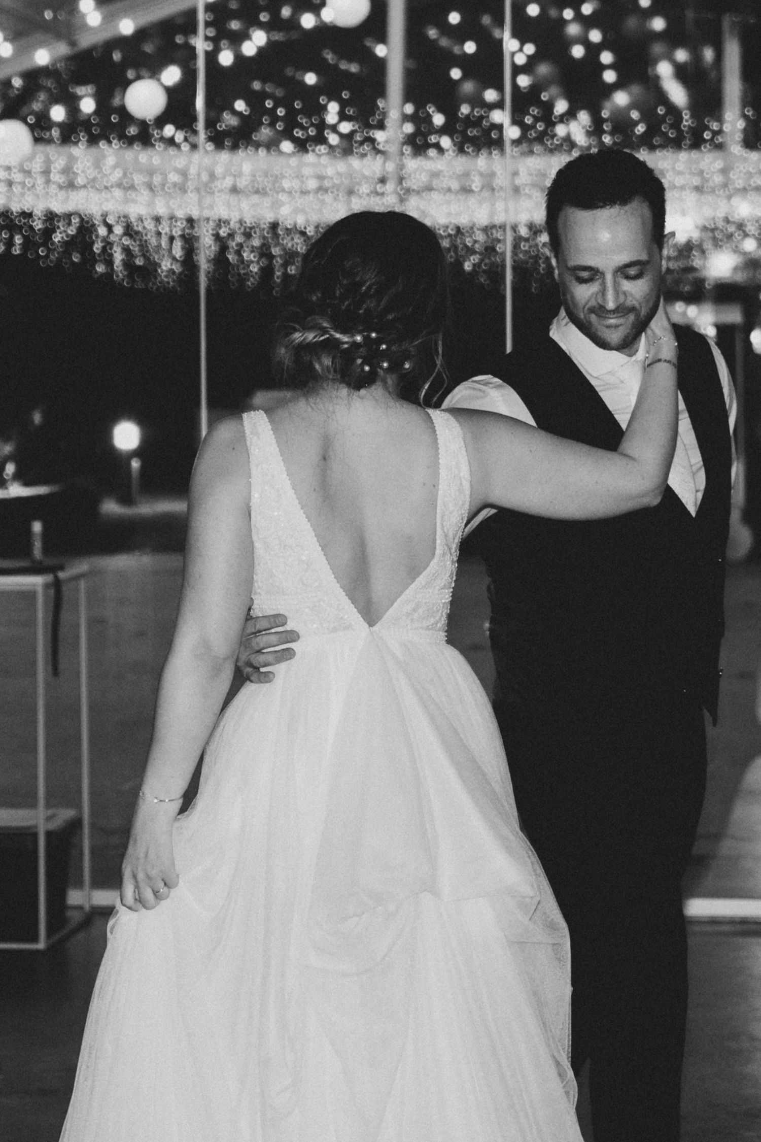 A couple shares their first dance at a wedding reception under twinkling lights and romantic decor.