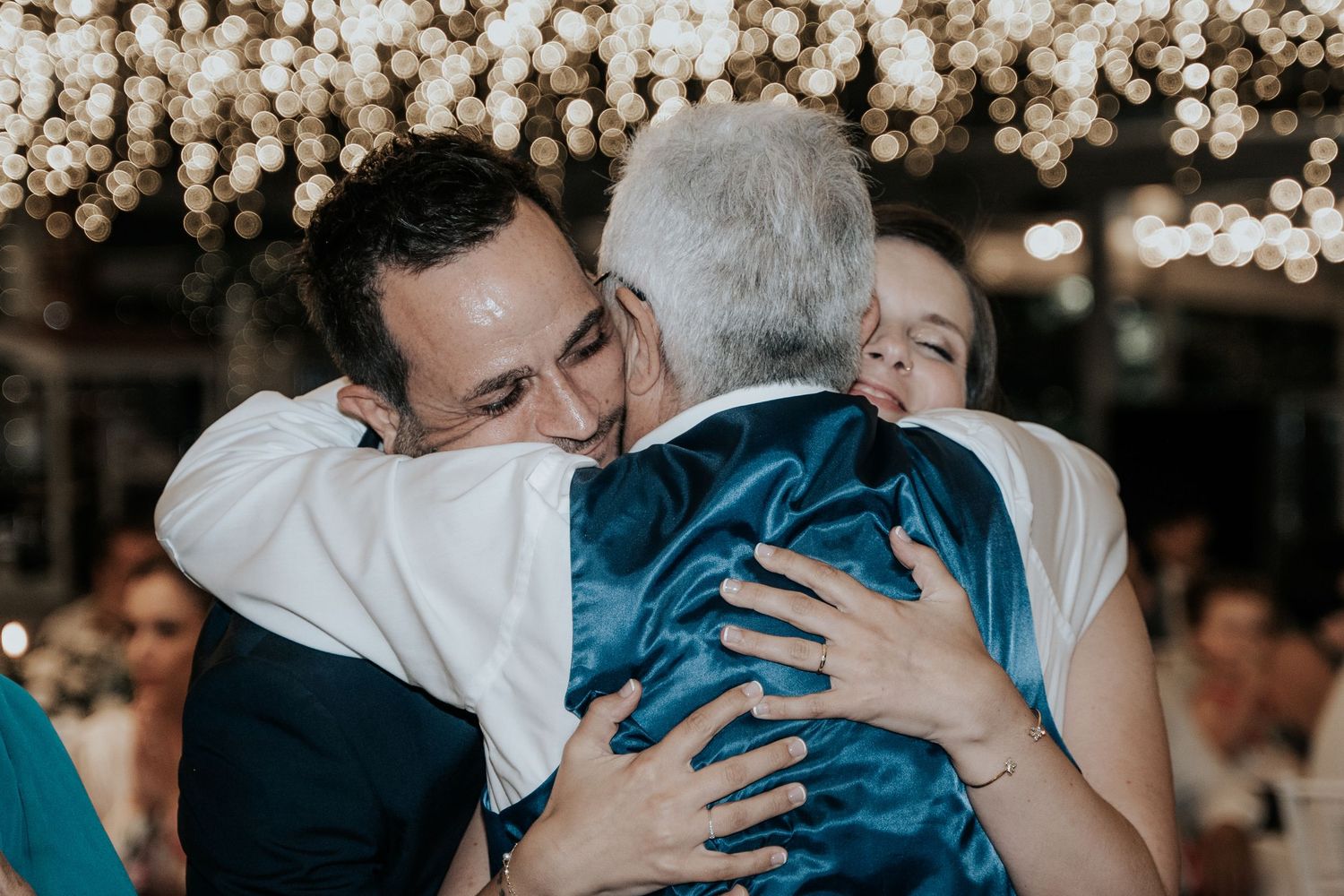 An emotional embrace shared between family members during a wedding celebration under glowing lights.