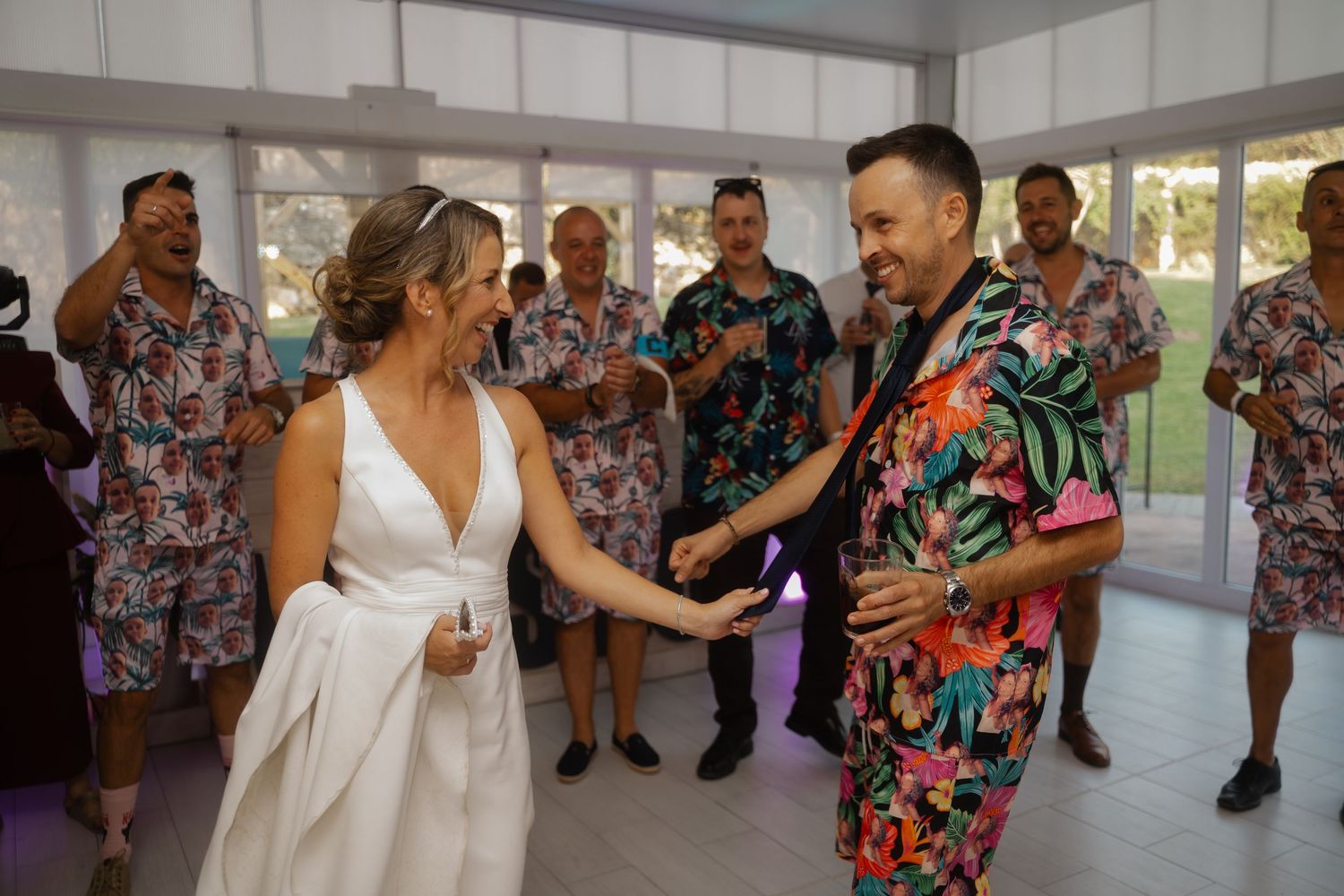 Wedding party guests dance and celebrate in matching floral print outfits while a bride in white dress joins the festivities.