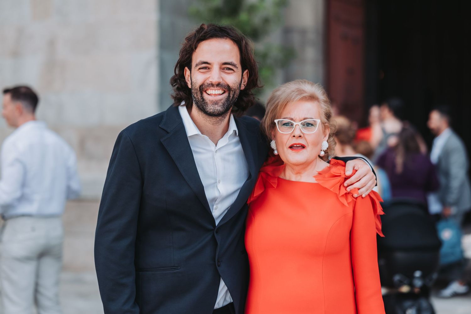 People in formal attire pose together at an event, with someone wearing a vibrant orange dress standing out.