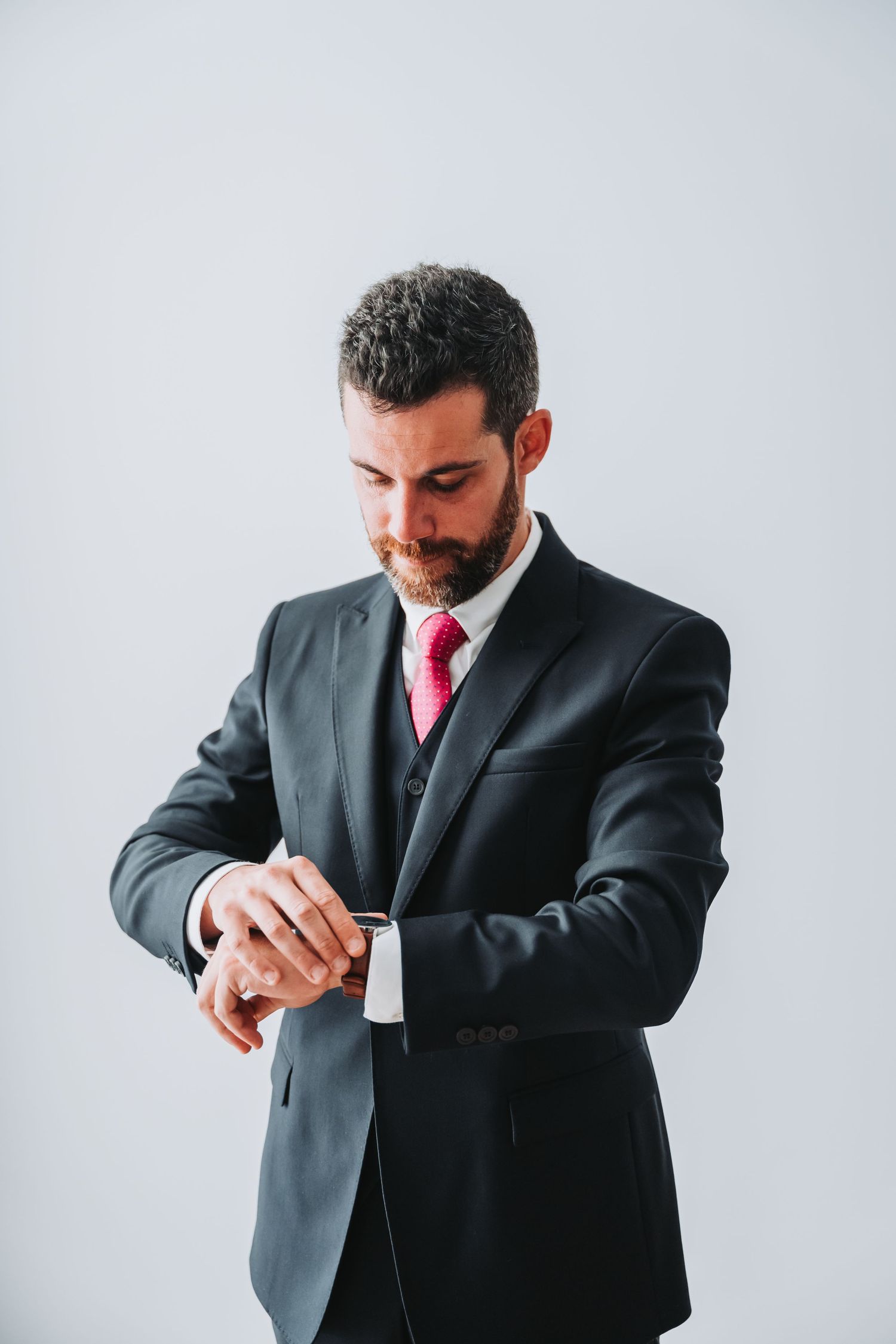 Professional in a dark suit and red tie checking his watch against a light background.