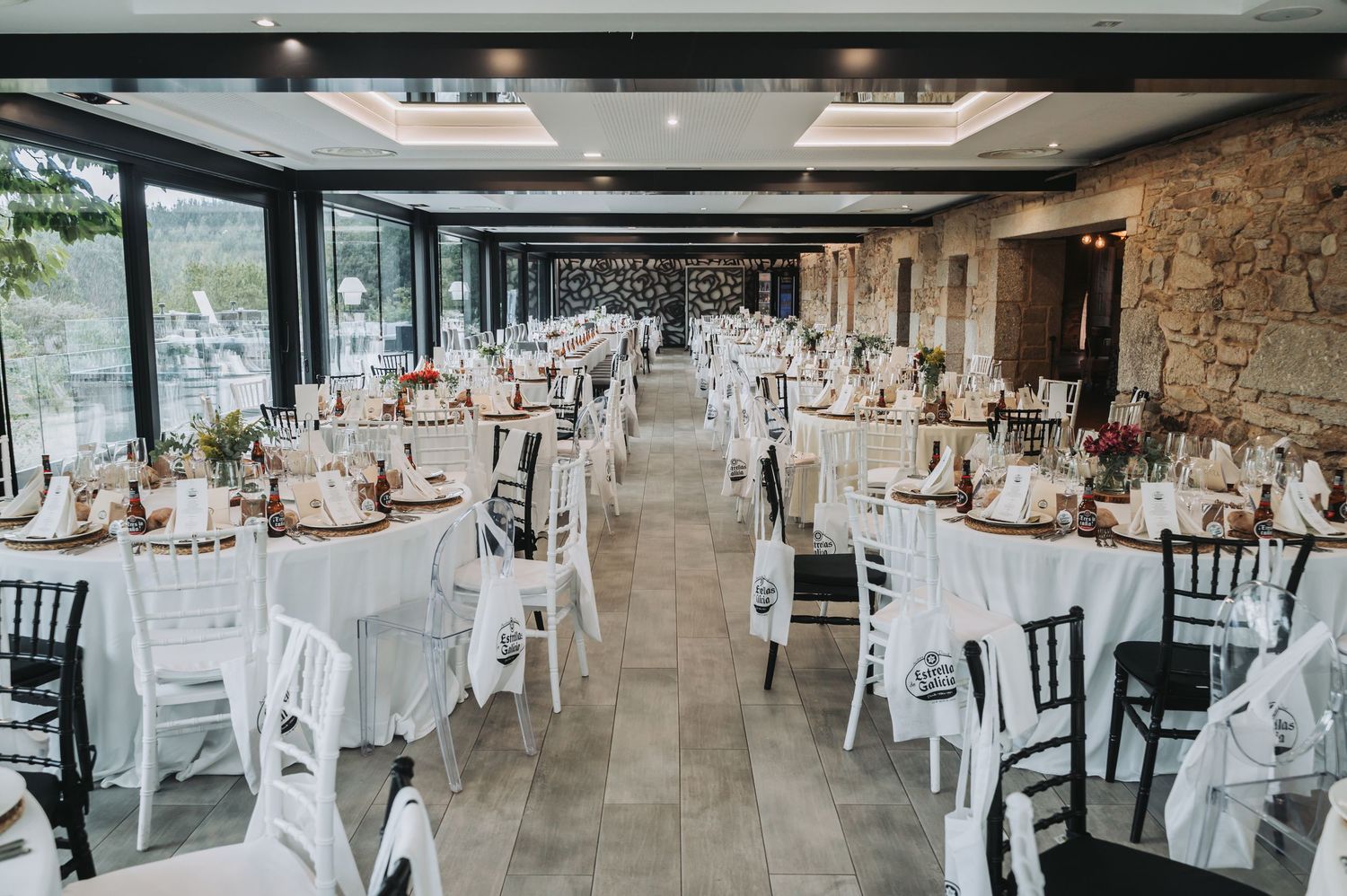 Elegant wedding reception venue with white tablecloths and rustic stone walls features panoramic window views.
