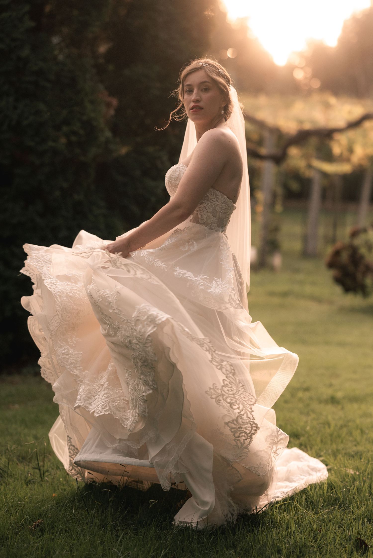 A wedding dress twirls gracefully in golden sunset light on a grassy lawn.