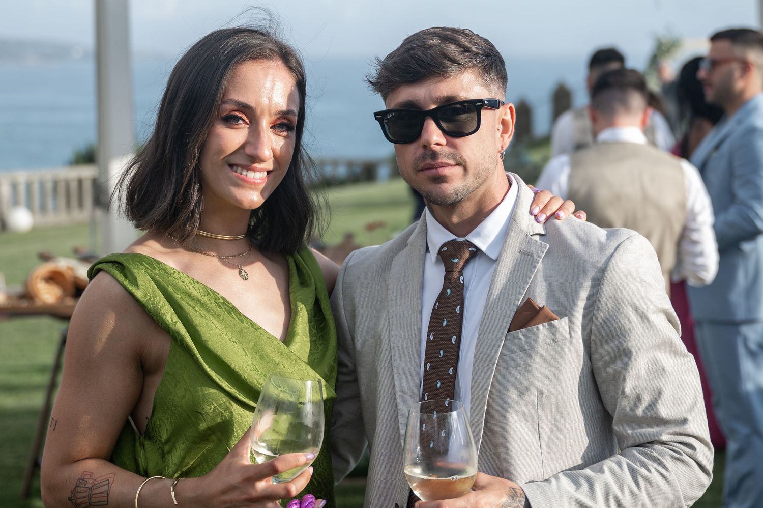 Wedding guests enjoy drinks and conversation at an outdoor reception by the water.