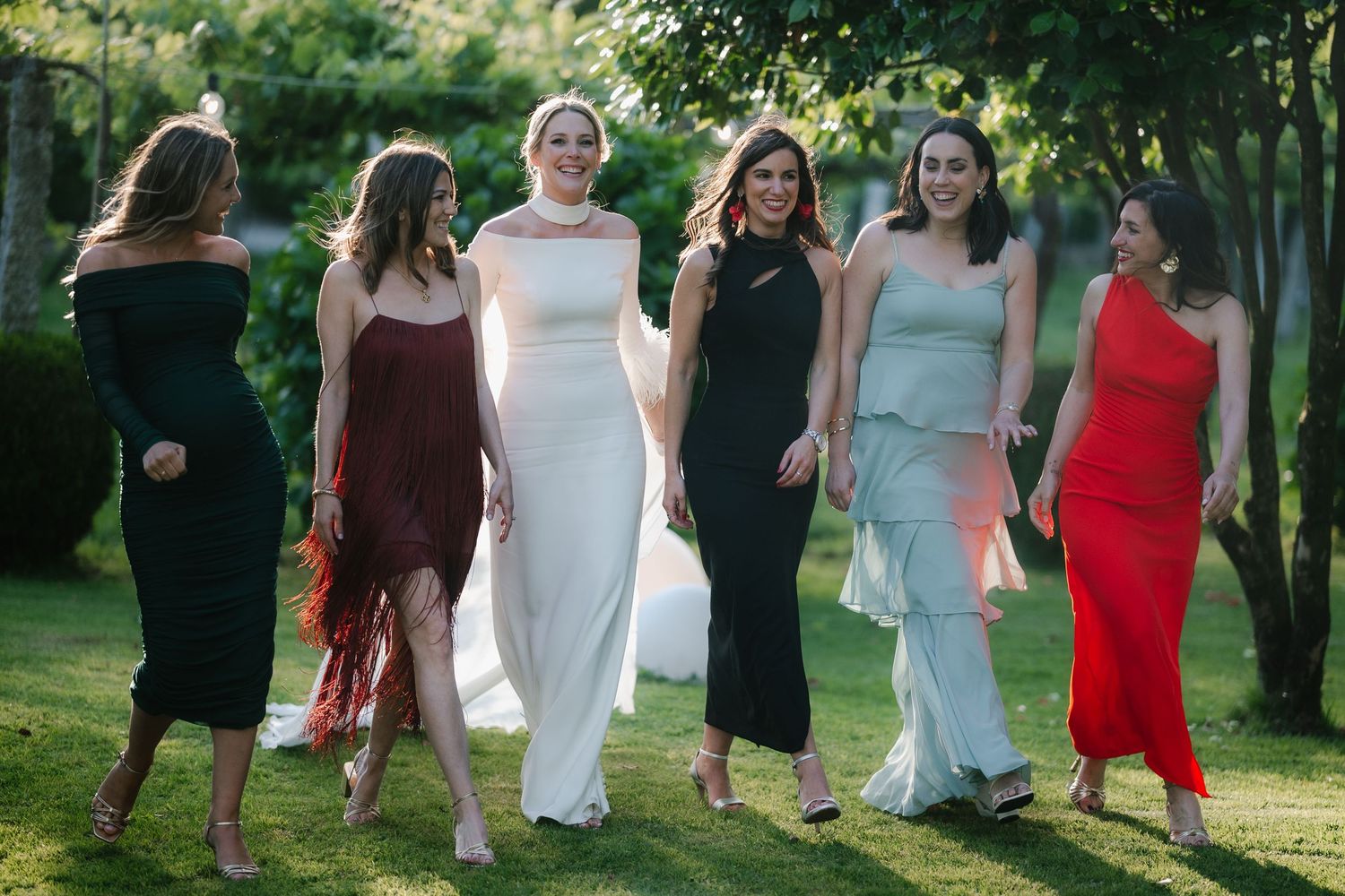 A group of people in formal attire walking together through a sunlit garden path during a summer event.