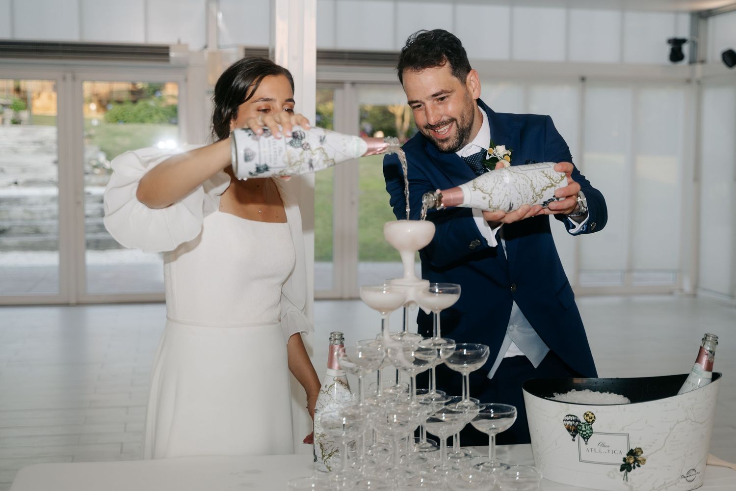 A couple shares a playful moment while toasting with champagne glasses in an elegant white venue.