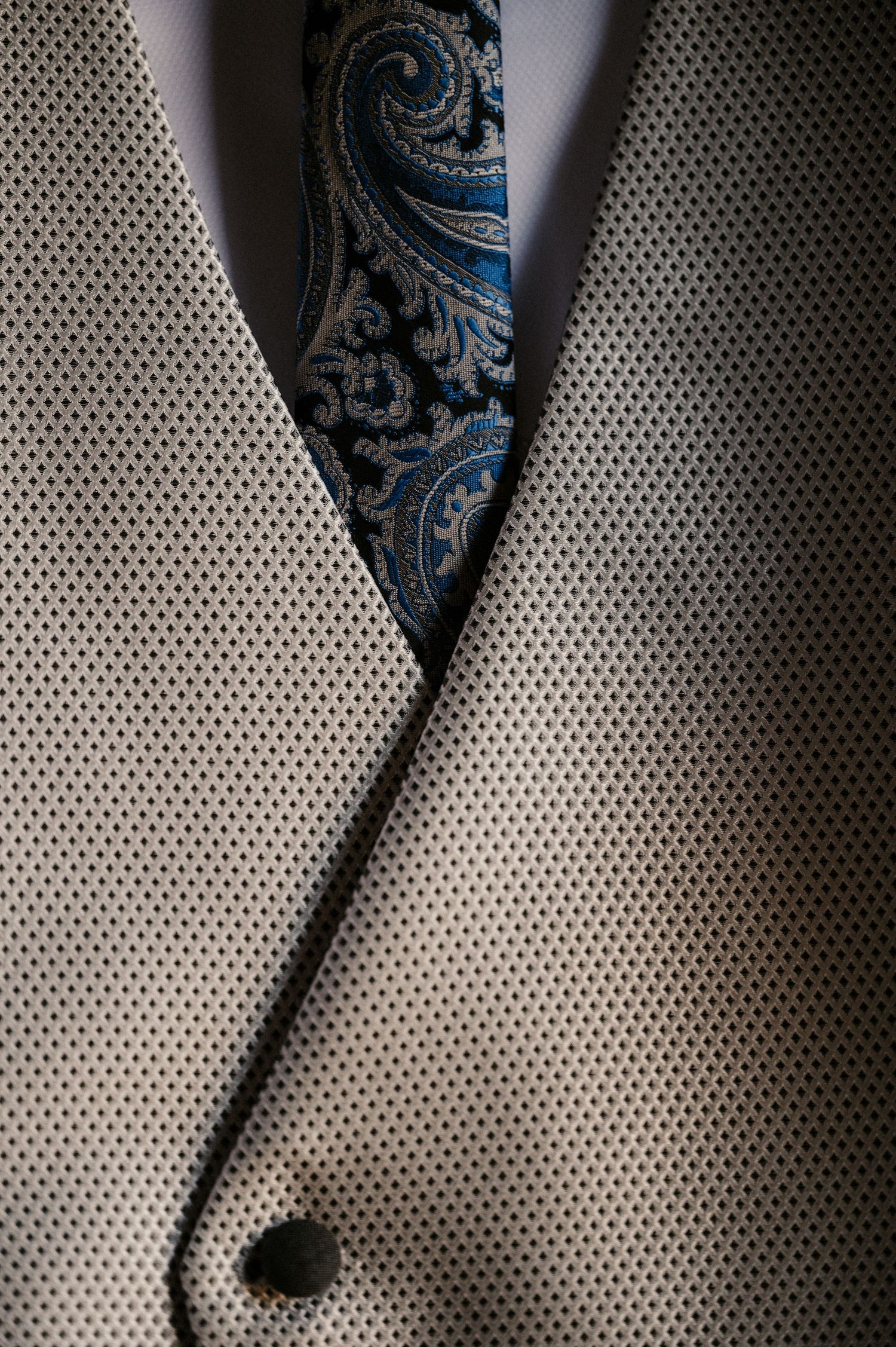 Close-up view of a formal gray suit jacket lapel with a blue and silver patterned silk tie.
