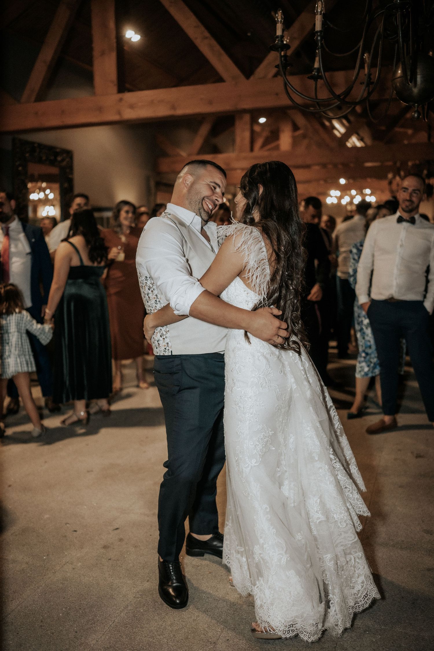 A couple shares a romantic dance at their wedding reception in a rustic barn venue with warm lighting.