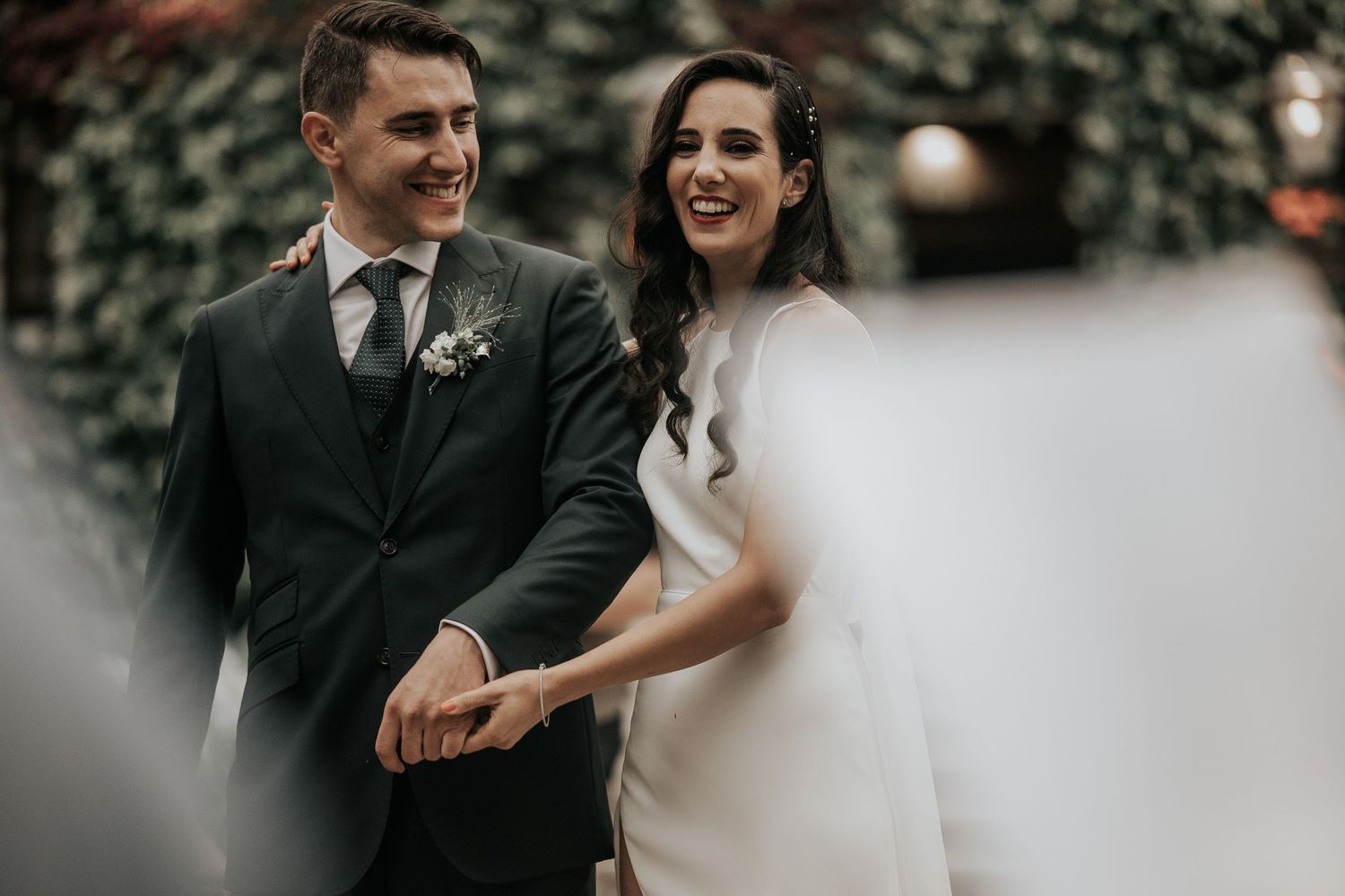 A couple shares a joyful moment during their wedding celebration in a moody, dark outdoor setting.