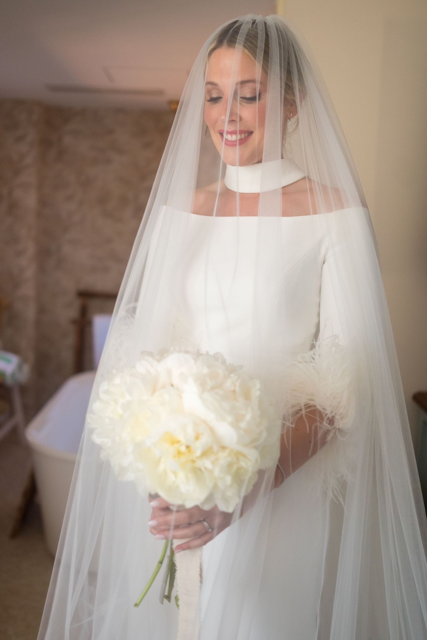 Bride in minimalist white wedding gown holding a cream-colored peony bouquet.