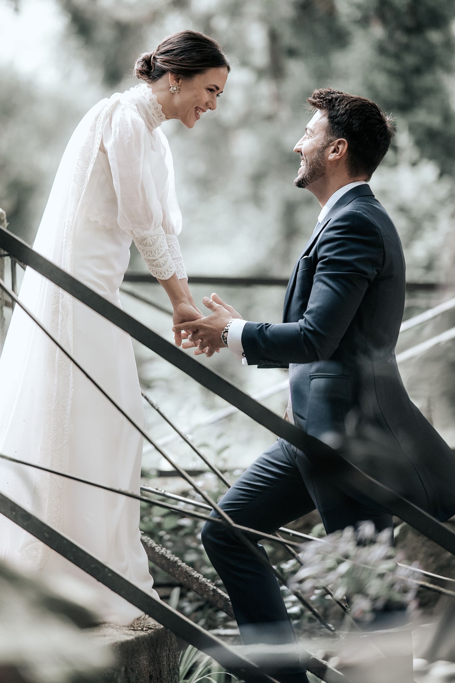 A couple shares a tender moment on outdoor steps, with the bride in white and groom in a dark suit.