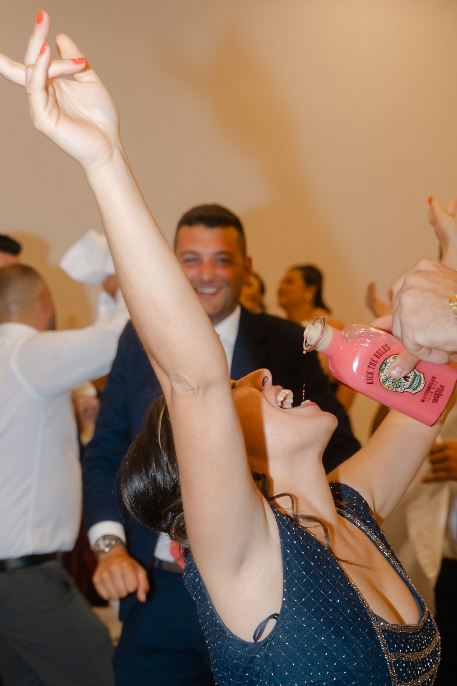 People on a dance floor raise their arms in celebration at what appears to be a party or wedding reception.