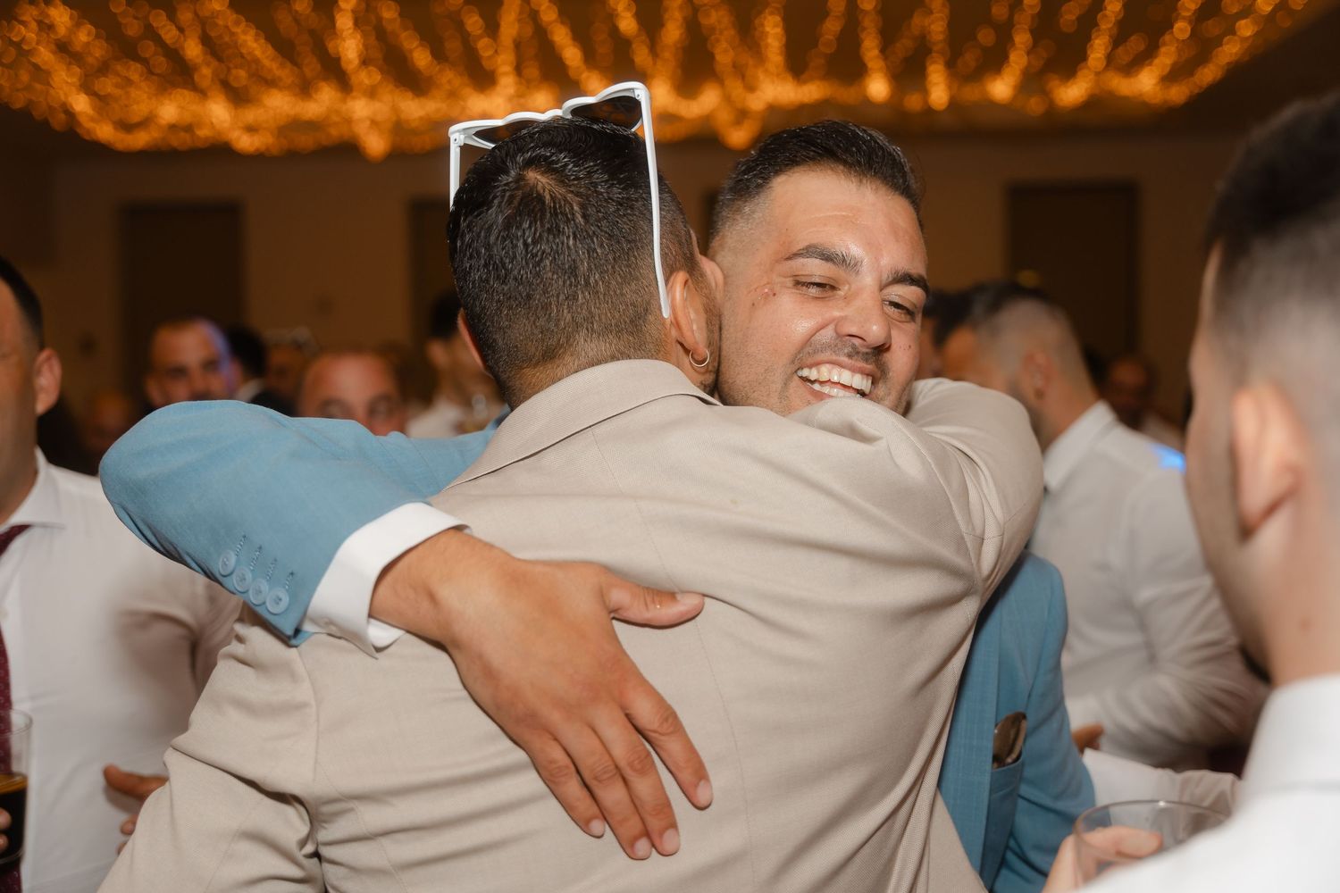 People embrace in an emotional group hug during what appears to be a wedding reception or celebration event.
