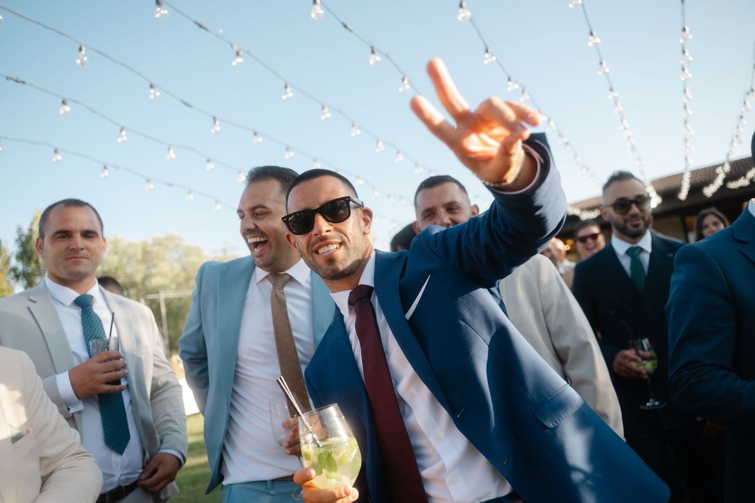 Groomsmen in suits and sunglasses pose together outdoors during a wedding celebration.
