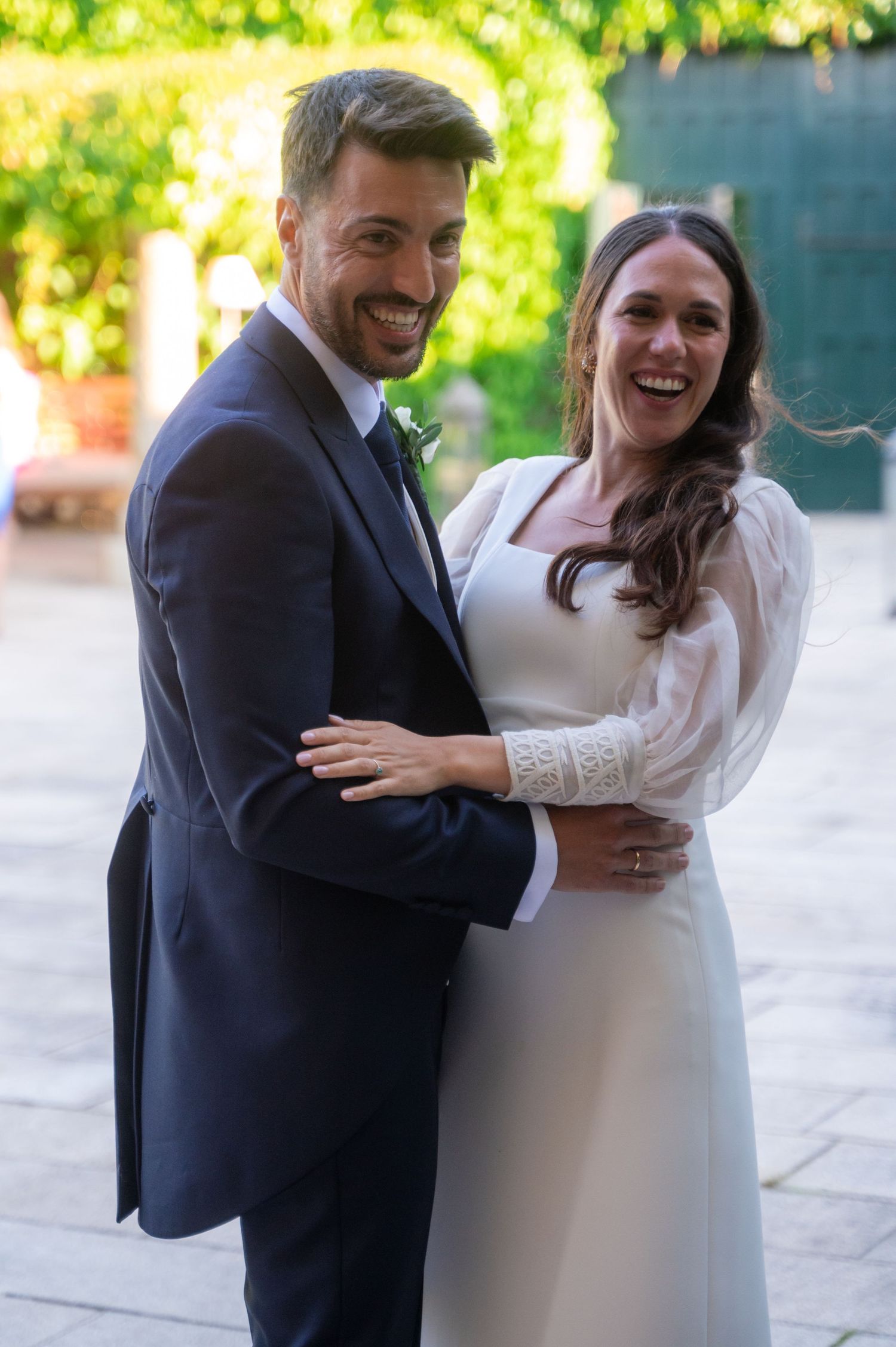 Couple in wedding attire laughing and dancing together in bright natural lighting.