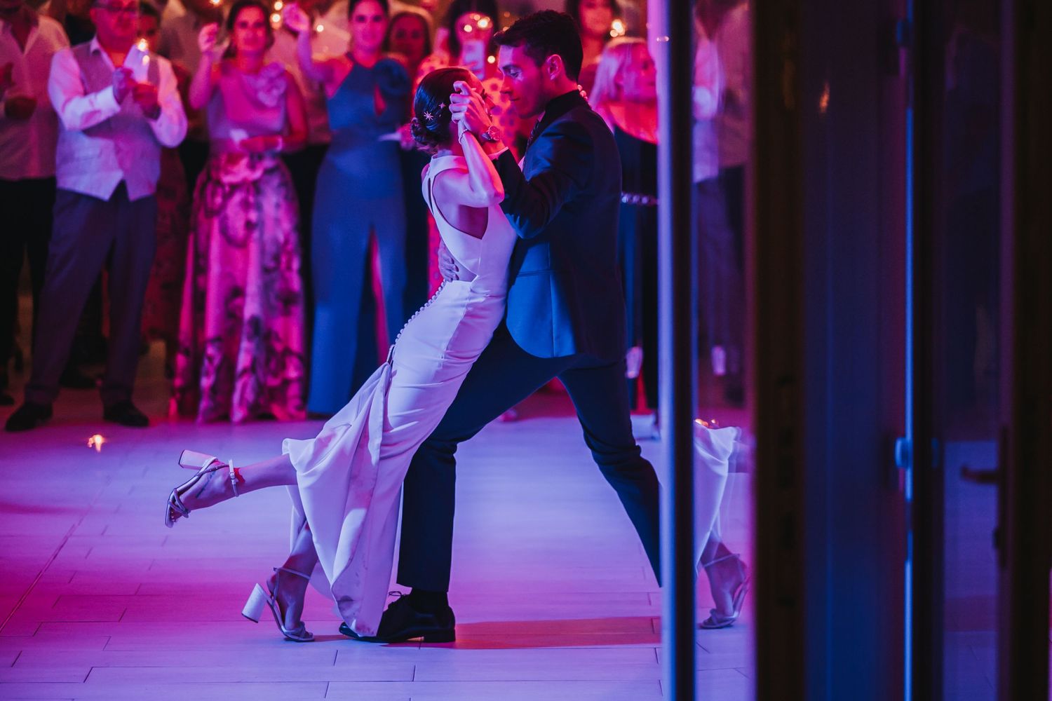Dancers performing elegant tango moves on a dance floor illuminated by vibrant purple and pink lighting.