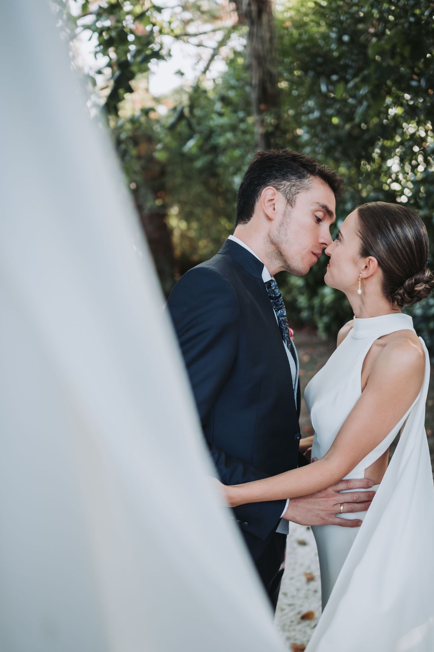 A romantic wedding couple shares an intimate kiss in a garden setting with soft lighting and greenery.
