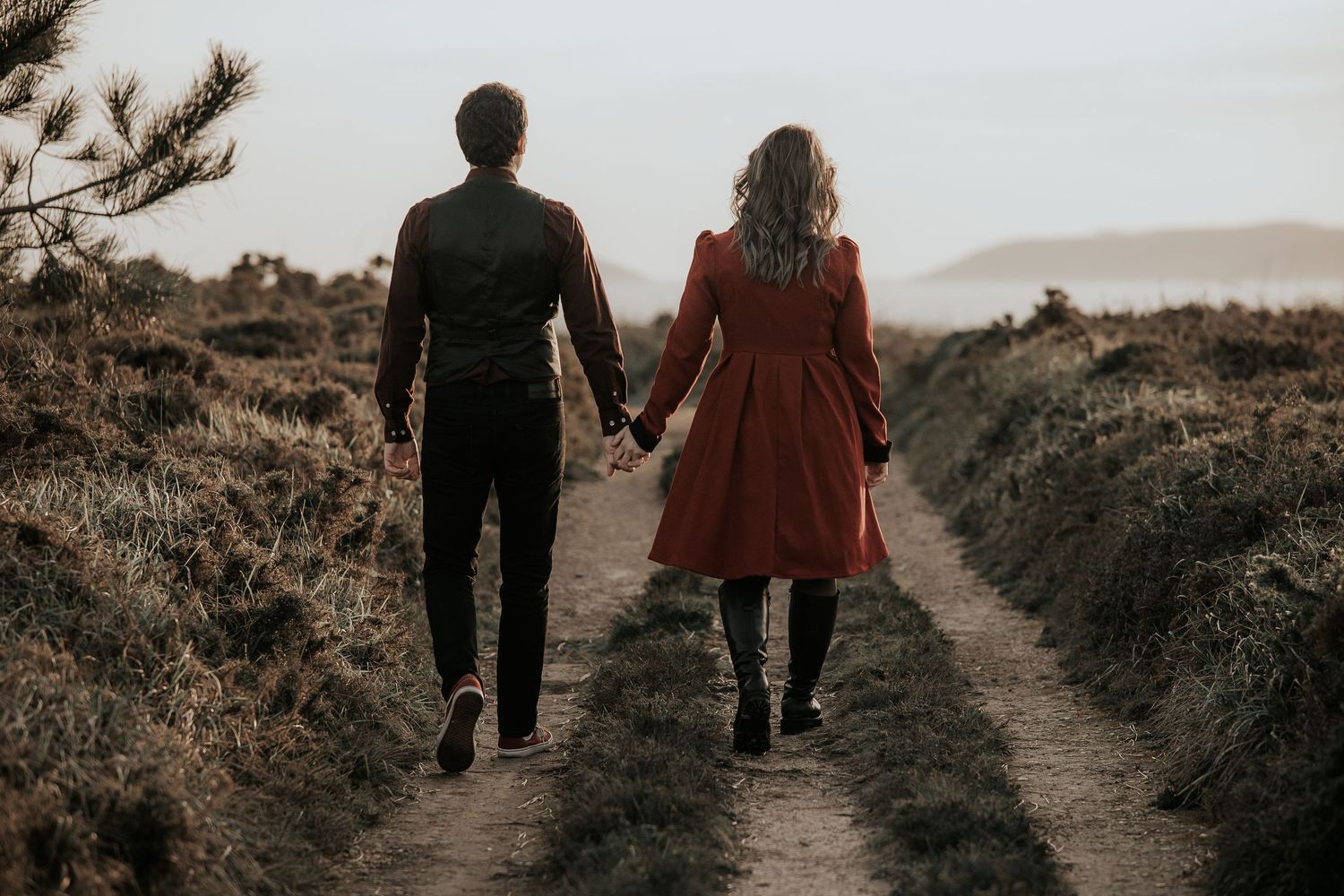 Two figures holding hands while walking along a rustic dirt trail in warm sepia tones.