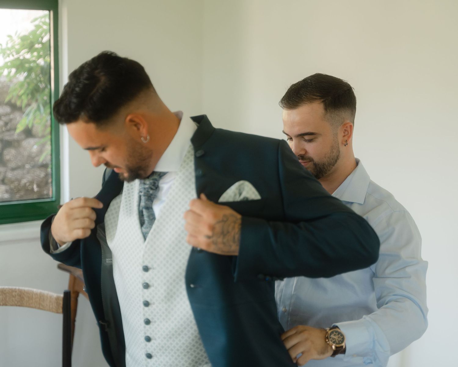 Several people in formal attire helping someone put on a suit jacket.