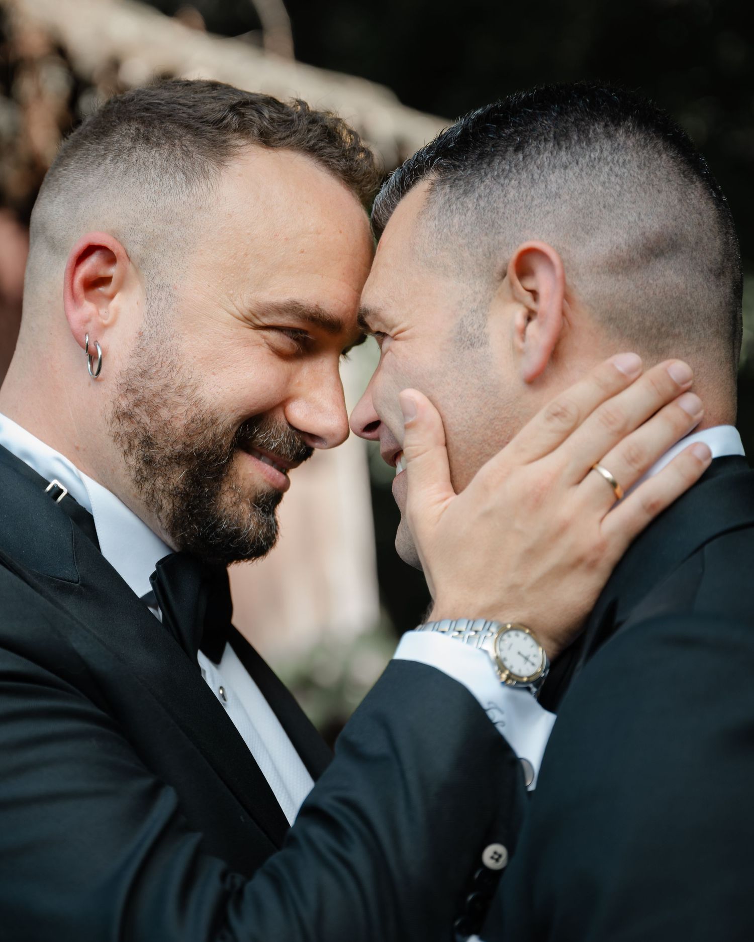 Two people in black tuxedos share an intimate moment during a wedding photoshoot.