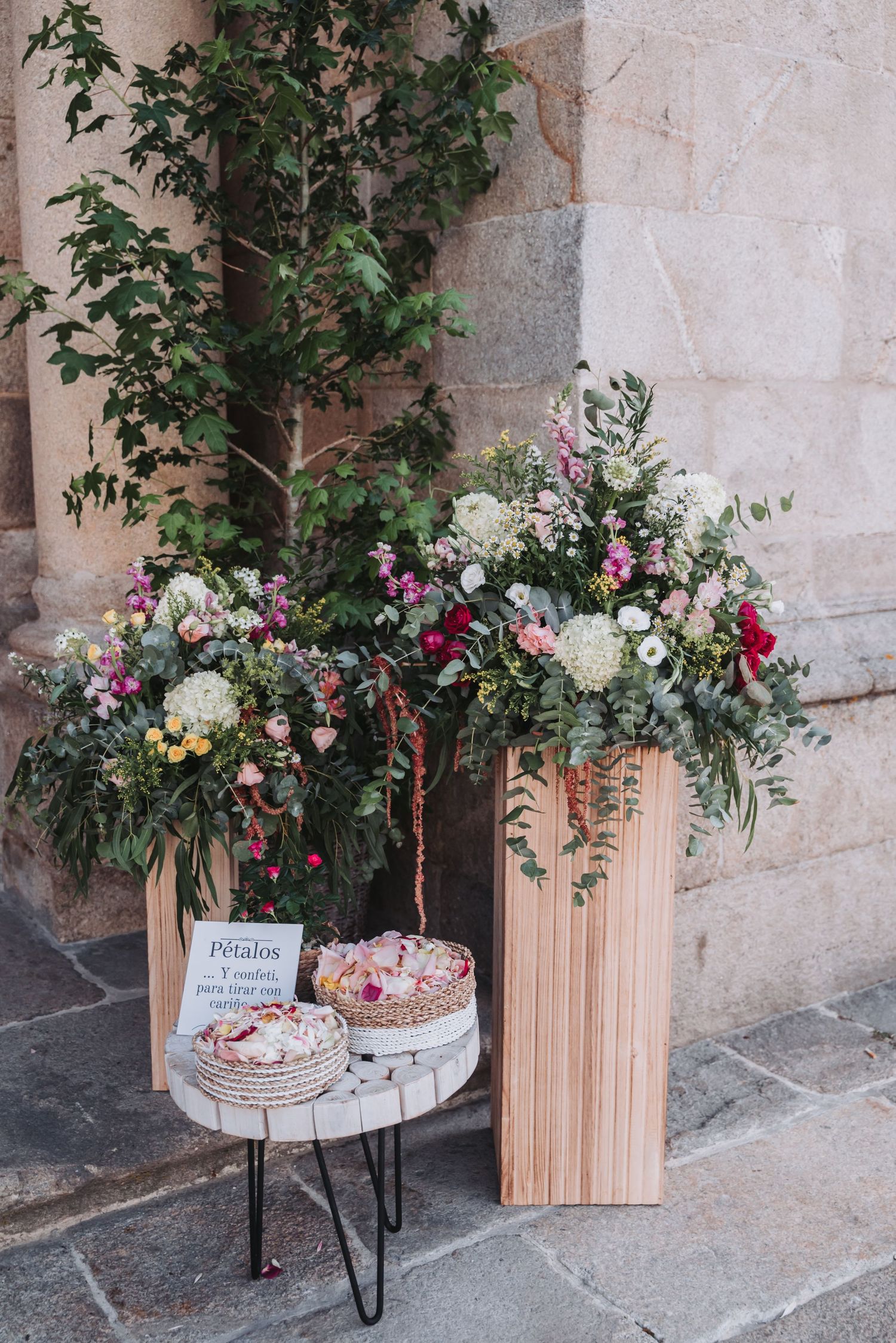 Elegant floral arrangements with pink and white flowers displayed alongside wooden decor elements against a stone wall.