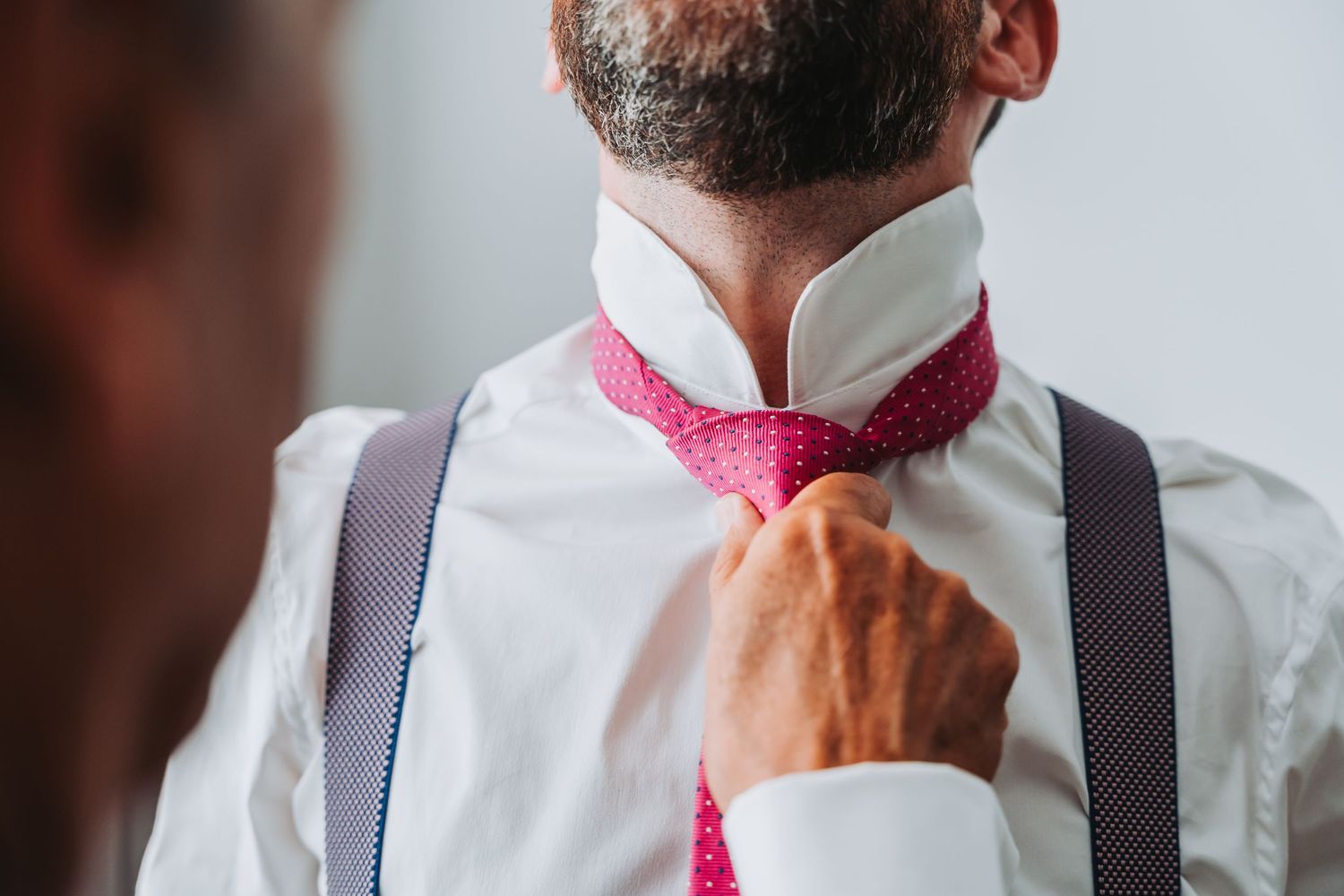 Close-up view of a pink bow tie and white dress shirt with black suspenders showing professional formal attire details.