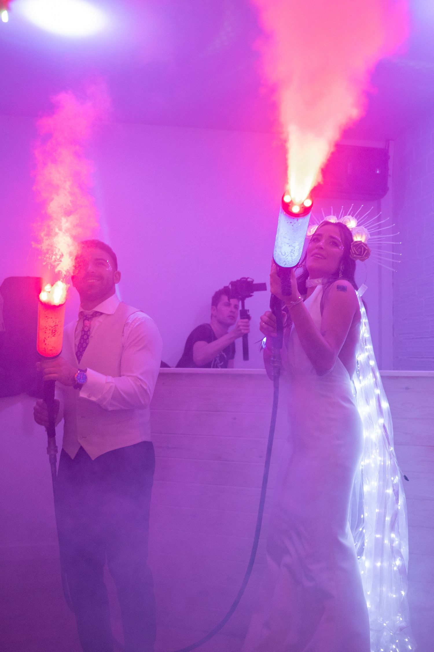 A DJ performs with illuminated CO2 cannons creating pink and purple smoke effects on stage during a show.
