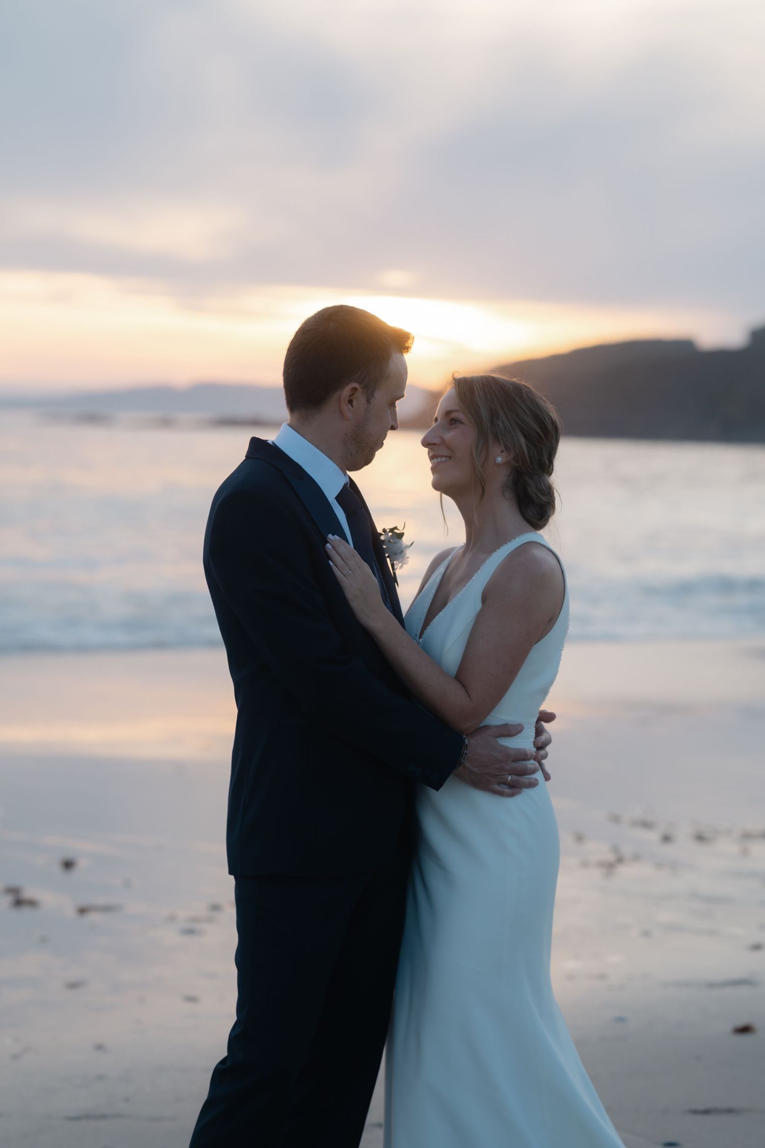 A romantic sunset beach wedding portrait with a couple embracing against the ocean backdrop.