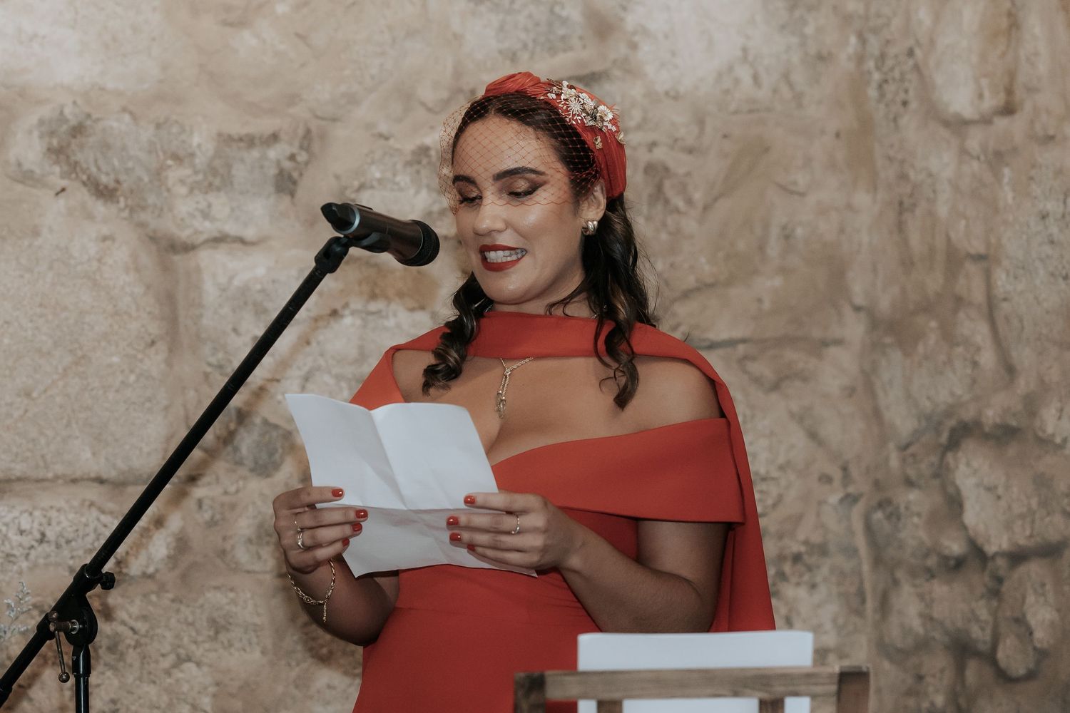 Wedding guest in red dress delivers emotional speech at reception microphone.