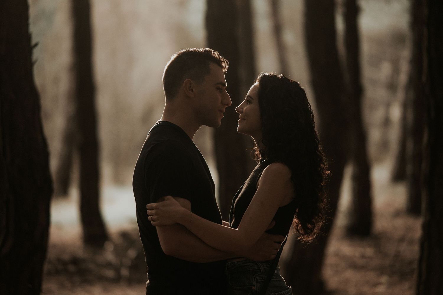 Silhouetted couple embracing in a moody forest setting with soft natural lighting.